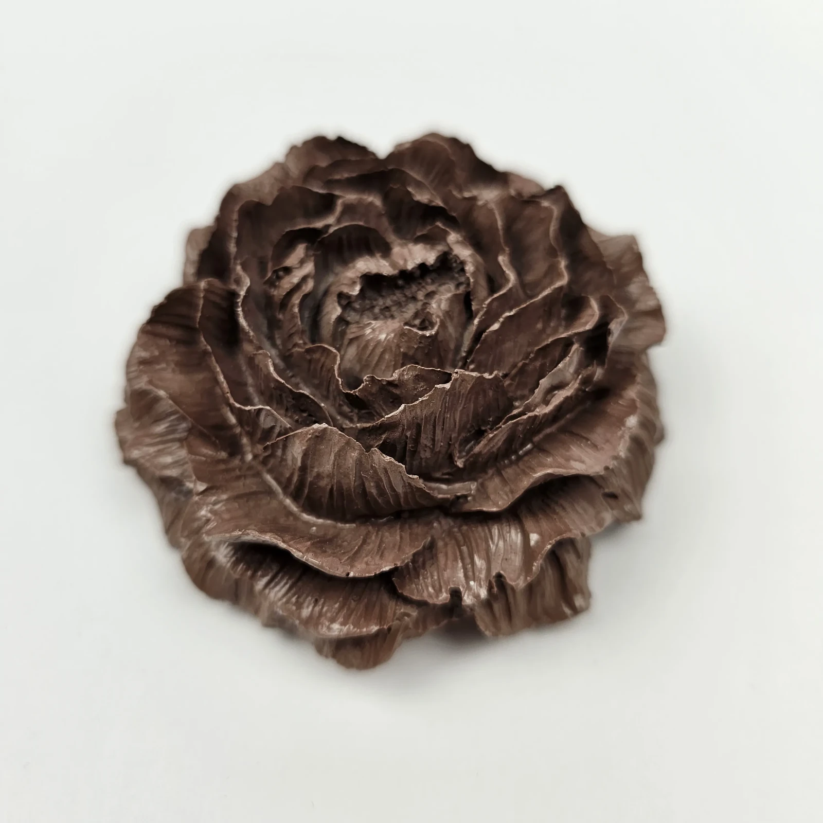 Ciemnobrązowa figurka kwiatowa w kształcie peonii leżąca na białym tle, dekoracja handmade.