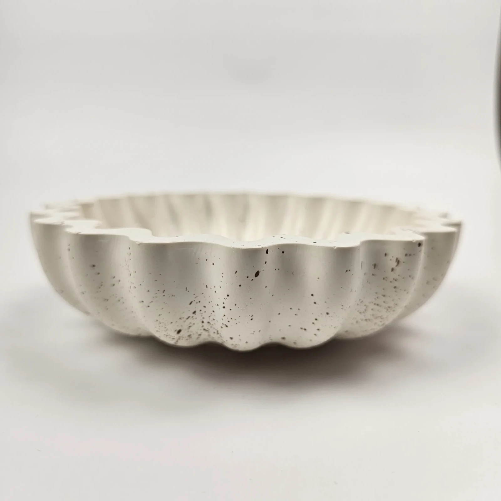 Profil ręcznie wykonanej, płytkiej miseczki ozdobnej z gipsu polimerowego, prezentującej pofałdowany kształt muszli.