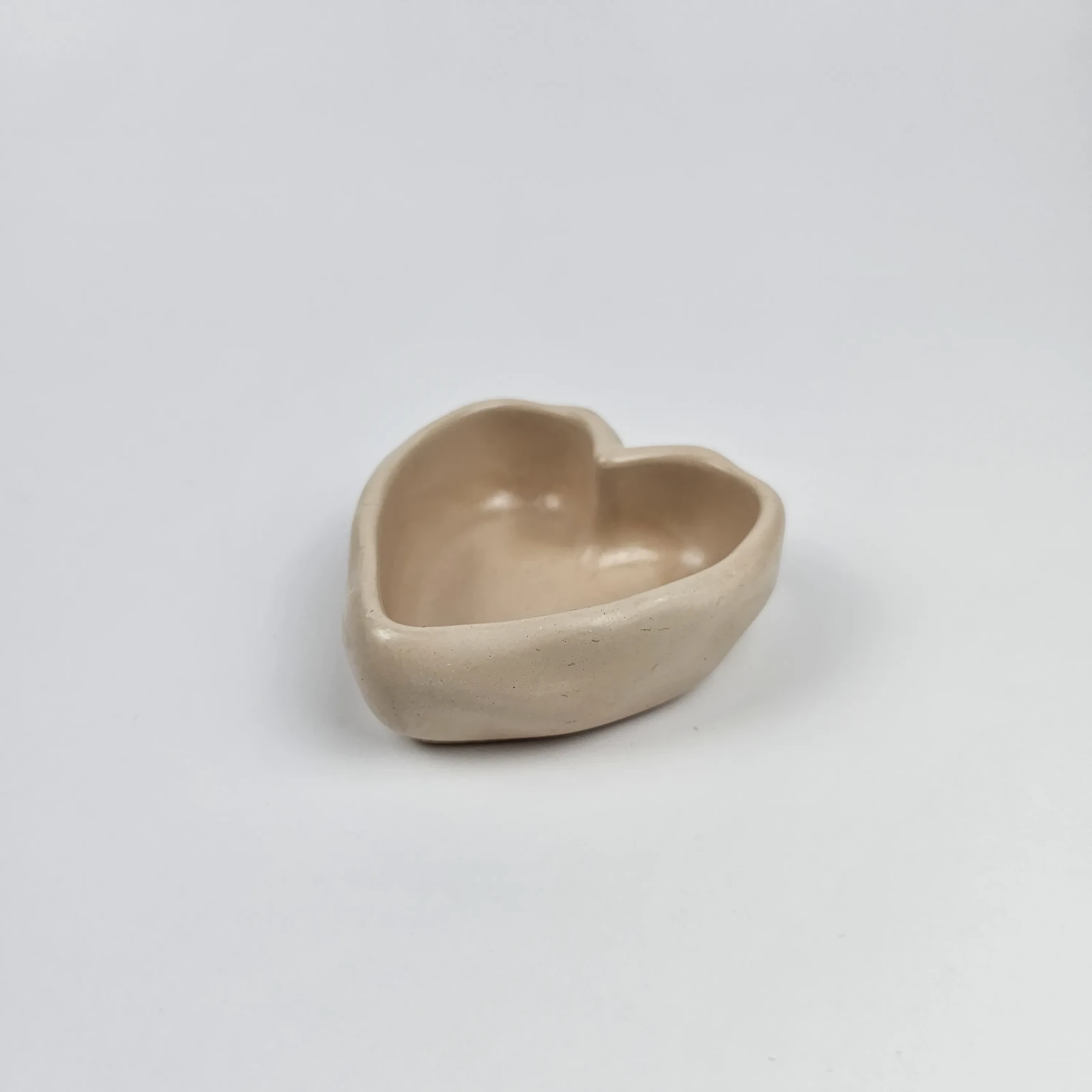 Mała, beżowa podstawka w kształcie serca z gipsu polimerowego widoczna z profilu, ukazująca gładką strukturę handmade.