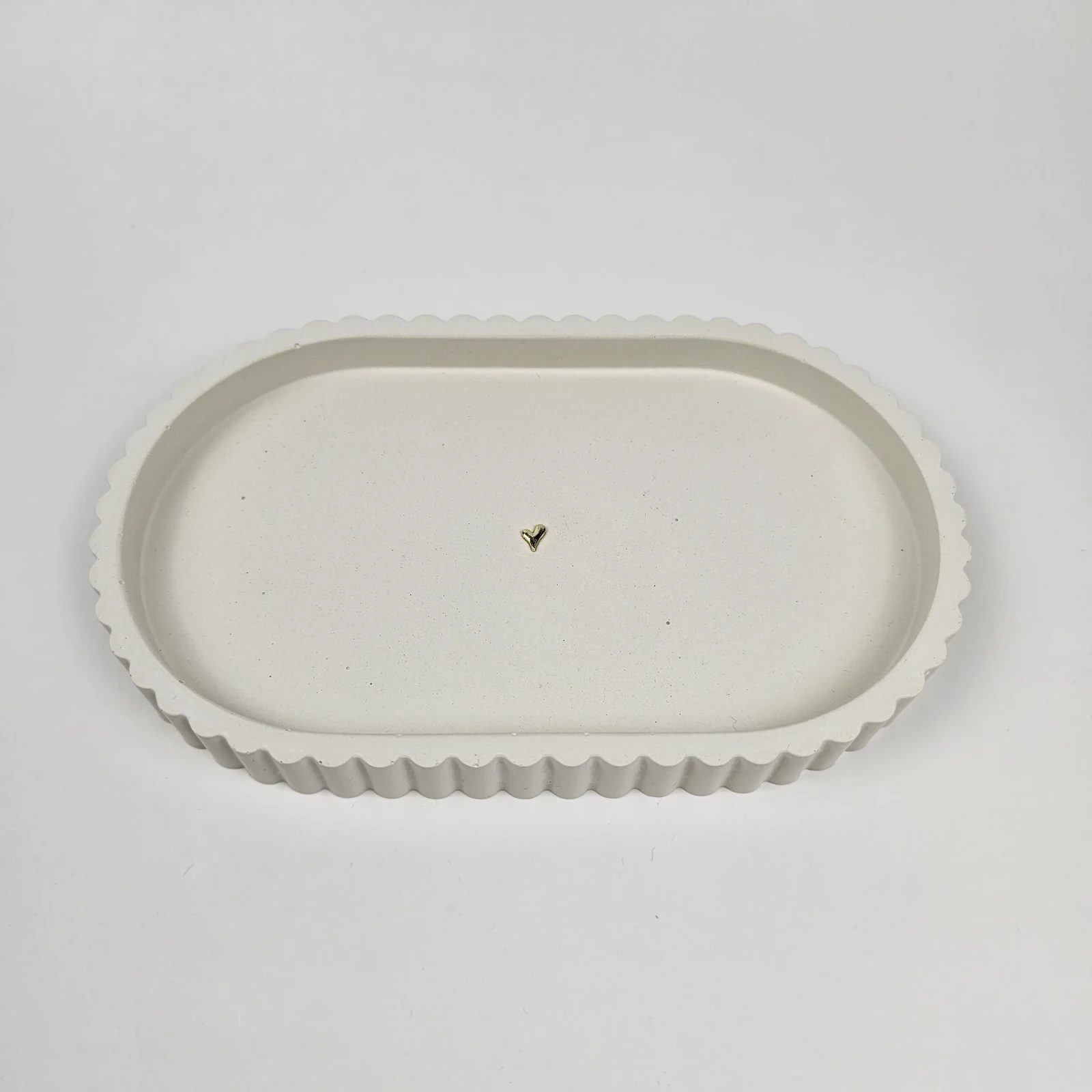 Beżowa owalna podstawka z gipsu polimerowego ze złotym serduszkiem na środku, idealna na biżuterię.