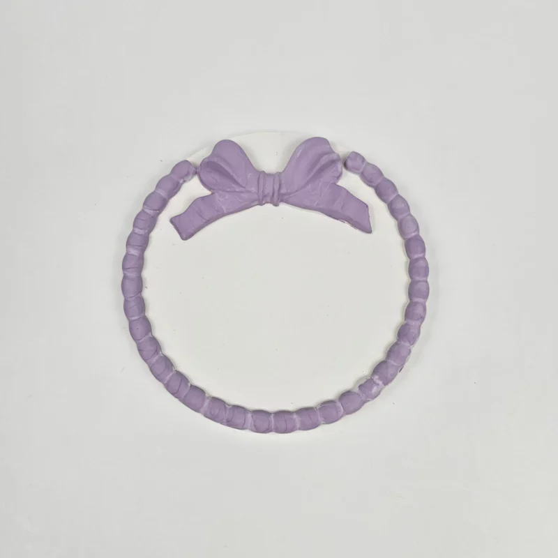 Biała okrągła podstawka z gipsu polimerowego z fioletową kokardą i ozdobnym rantem z koralików.