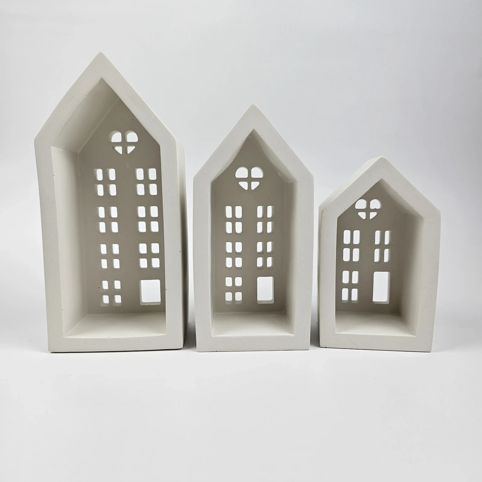 Zestaw trzech białych świeczników w kształcie domków z gipsu polimerowego z wyciętymi sercami i okienkami